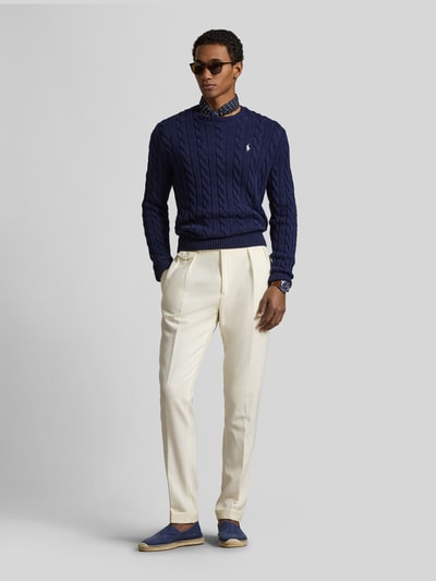 Męski model nosi Regular Fit Strickpullover aus reiner Baumwolle od Polo Ralph Lauren w granatowym, wzór warkoczowy, logo, okrągły dekolt, dzianina, perspektywa całopostaciowa z przodu.