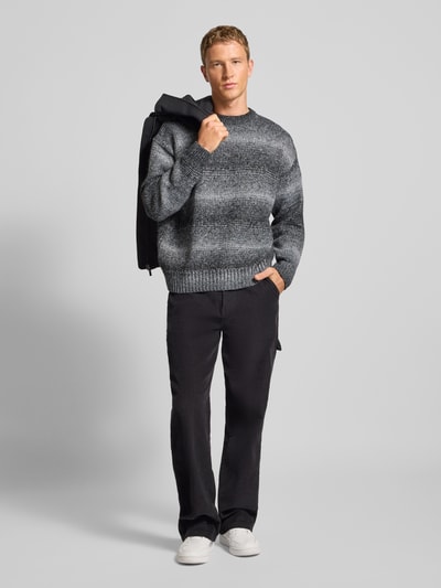Męski model nosi Oversized Strickpullover mit gerippten Abschlüssen von Pegador, melanż szaro-czarny, okrągły dekolt, widok całej sylwetki z przodu.