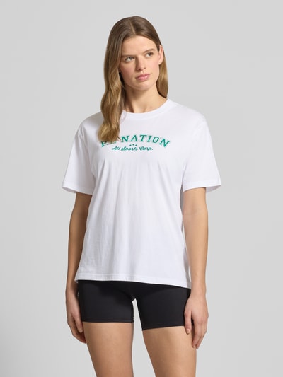 Frauenmodel trägt T-Shirt mit Logo-Print und Rundhalsausschnitt von P.E Nation aus Reine Baumwolle im Relaxed-Fit, Rückenlänge 64 cm, Ganzkörperansicht von vorne.