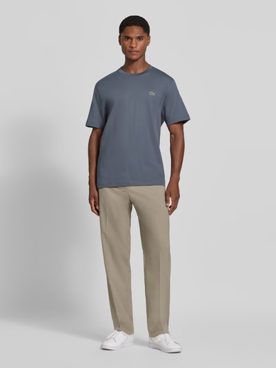 Männermodel trägt Regular Fit T-Shirt aus reiner Baumwolle von Lacoste in Blau, kombiniert mit hellen Hosen, Ganzkörperansicht von vorne. Herren T-Shirt von Lacoste