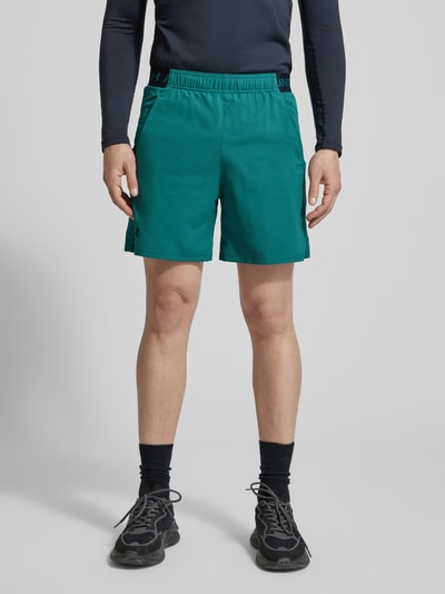 Mężczyznamodel nosi Straight Fit Shorts mit Logo-Print Modell 'Vanish' od Under Armour, zielony kolor, elastyczny pas, kieszenie, Szerokość w rozmiarze M: 38 cm, długość nogawki wewnętrznej: 15 cm, Ganzkörperansicht von vorne.