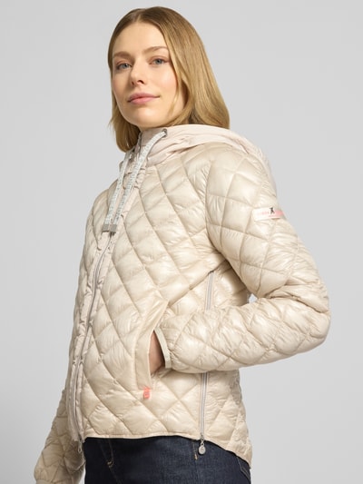 Frauenmodel trägt Regular Fit Jacke in Stepp-Optik Modell 'YOSIE' von Frieda & Freddies, Beige, mit Kapuze, Tunnelzug, Eingrifftaschen, Reißverschluss, Logo-Applikation, elastische Ärmelabschlüsse, Ganzkörperansicht von vorne.