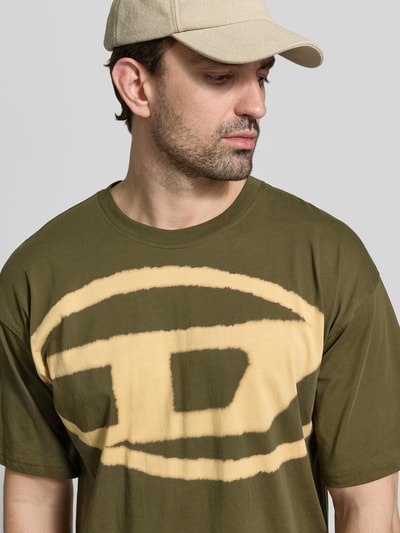 Männermodel trägt Regular Fit T-Shirt mit Logo-Print von Diesel in Olivgrün und Beige, Reine Baumwolle, Nahaufnahme Oberkörper.