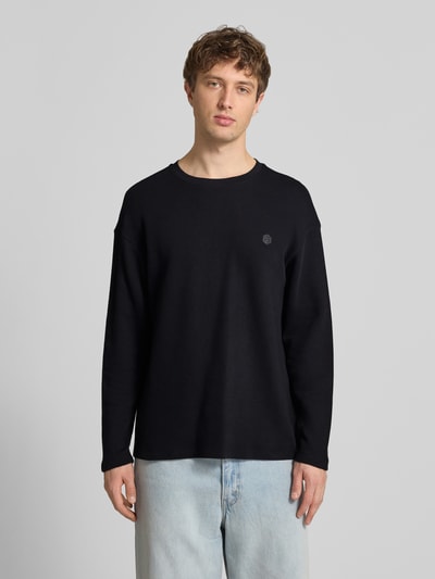Männermodel trägt Longsleeve aus Baumwolle Modell 'FILLIP' von Blend, schwarze Farbe, Gerader-Schnitt, Label-Detail, Ganzkörperansicht von vorne. Rückenlänge bei Größe M: 70 cm.