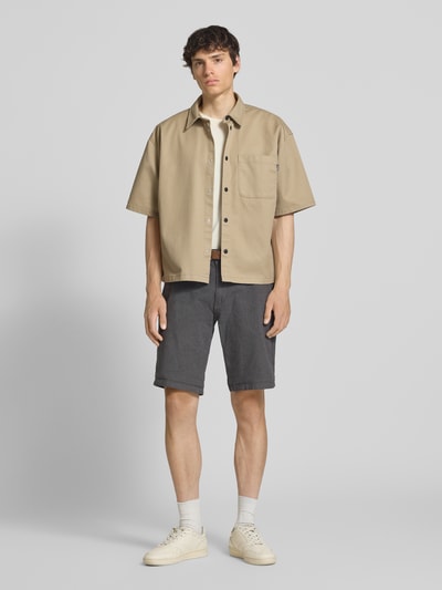 Männermodel trägt Bermudas mit Gürtel und Eingrifftaschen Modell 'NEBRASKA' von Redefined Rebel, Baumwoll-Mix mit Stretch-Anteil, Ganzkörperansicht von vorne.