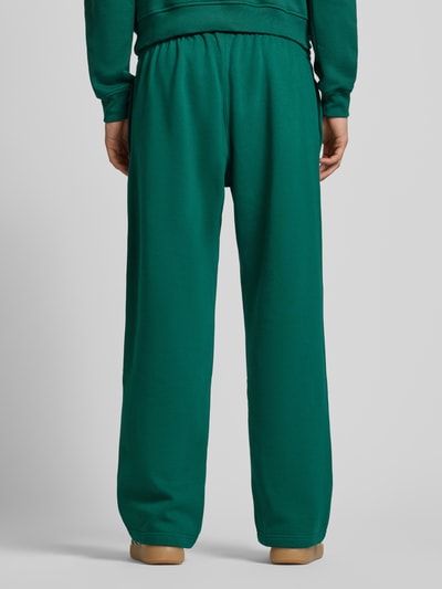 Männermodel trägt Wide Fit Sweathose mit elastischem Bund von adidas Originals in Dunkelgrün mit Logo-Stitching, Baumwoll-Mix, Ganzkörperansicht Rückansicht.