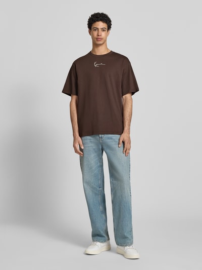 Männermodel trägt Regular Fit T-Shirt mit Logo-Stitching von KARL KANI in Braun, Rundhalsausschnitt, Kurzärmelig, Ganzkörperansicht von vorne, Rückenlänge bei Größe M 74 cm.