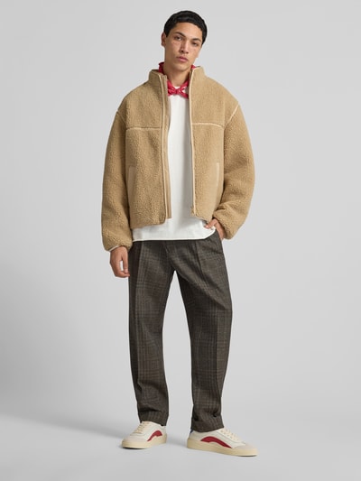 Männermodel trägt Sneaker mit Schnürverschluss von Dsquared2 in Beige und Rot, strukturierte Sohle, Ganzkörperansicht von vorne.