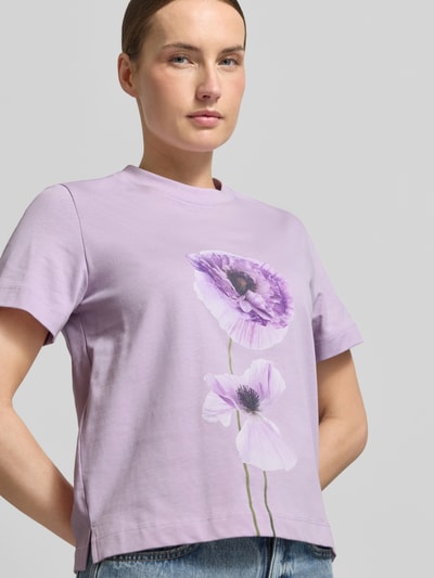 Modelka kobieca nosi T-shirt z motywem FIORE od Stefanel, jasnofioletowy, bawełna, prosty krój, nadruk kwiatowy, ujęcie z przodu, zbliżenie na górną część ciała.