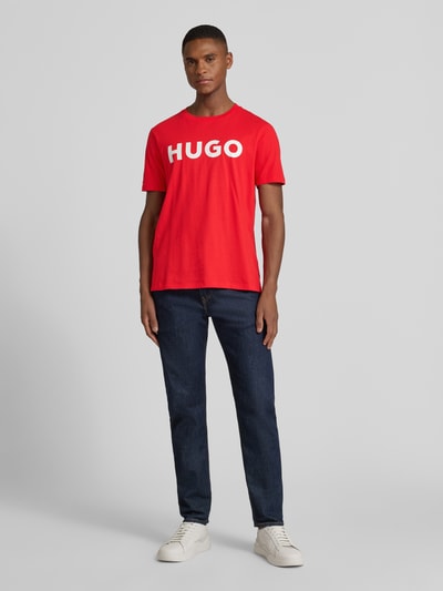Männermodel draagt T-Shirt met Label-Schriftzug Modell 'DULIVIO' van HUGO, rood katoen, rechte pasvorm, unidesign, voorkant volledig, ganzkörperansicht van voren.