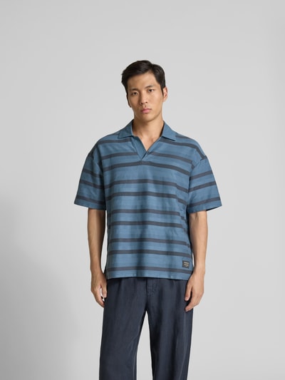 Männermodel trägt Oversized Poloshirt mit Logo-Patch von MAISON KITSUNÉ aus Reiner Baumwolle, Oversized-Fit, gestreiftes Kurzärmeliges Design, Ganzkörperansicht von vorne.