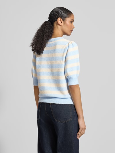 Frauenmodel trägt Regular Fit Strickpullover mit Crew Neck Modell 'DOFFY' von Vero Moda, Optik: Unifarben, Strickoptik, Label-Stitching-Applikation, Rundhals, 1/2-Arm, gerippte Abschlüsse, Materialverarbeitung: Strick, Farben Hellblau und Creme, Ganzkörperansicht Rückansicht.