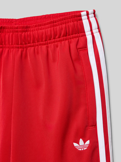 Produktfoto, Trainingshose mit Label-Stitching von adidas Originals in Rot mit weißen Streifen, Regular Fit, elastischer Bund, Eingrifftaschen