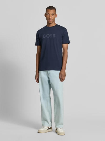 Männermodel trägt dunkelblaues Regular Fit T-Shirt aus reiner Baumwolle Modell 'Te_Logo' von BOSS Orange, helle Jeans, Ganzkörperansicht von vorne.