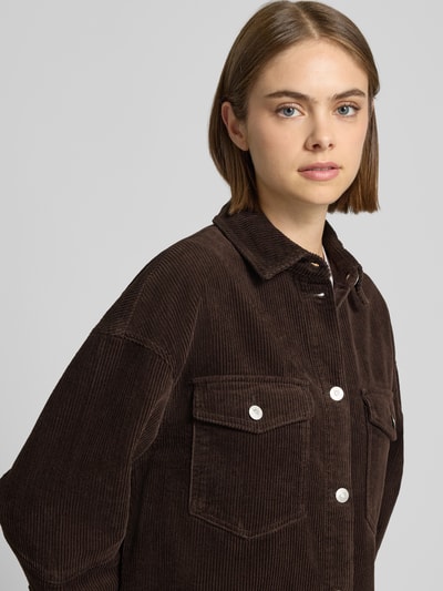 Frauenmodel trägt Loose Fit Hemdjacke aus reiner Baumwolle Modell 'TIGGY' von ONLY in dunkelbraunem Cord mit Brusttaschen, Nahaufnahme Oberkörper.