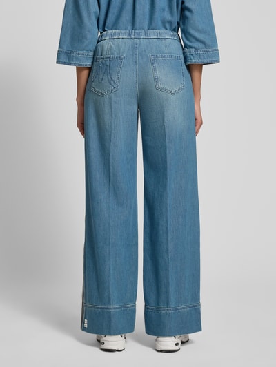 Frauenmodel trägt Wide Fit Jeans mit Lyocell-Anteil von Marc Cain, blauer Baumwoll-Lyocell-Mix, sichtbare Bügelfalten, elastischer Bund mit Tunnelzug, Eingriff- und Gesäßtaschen, Jeans-Look, Ganzkörperansicht Rückansicht.