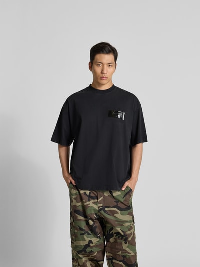 Männermodel trägt T-Shirt aus reiner Baumwolle von VETEMENTS in Schwarz mit Label-Detail, Relaxed-Fit, Rundhalsausschnitt, kurzärmelig, Ganzkörperansicht von vorne.