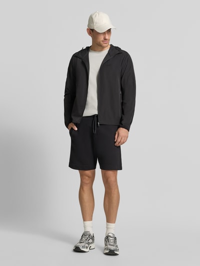Männermodel trägt Regular Fit Trainingsjacke mit Label-Print Modell 'OW_Airynix JT HD 2' von BOSS Green in Schwarz, Ganzkörperansicht von vorne.