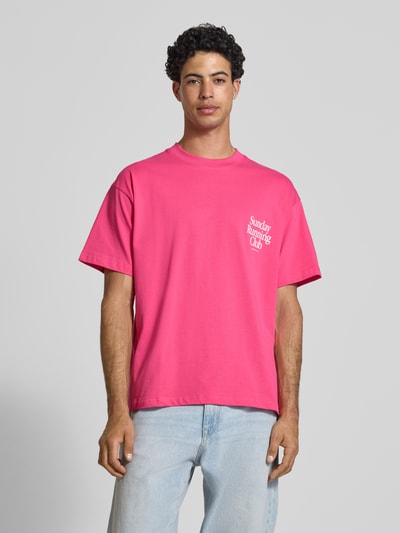 Männermodel trägt T-Shirt mit Statement-Print Modell 'Sunday Running Club' von ANOTHER COTTON LAB in Pink, reine Baumwolle, Boxy Fit, Rundhalsausschnitt, Ganzkörperansicht von vorne.