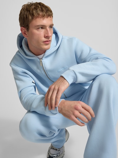 Männermodel trägt Regular Fit Sweatjacke mit Reißverschluss von Review in Hellblau aus Baumwoll-Mix, Logo-Print, Kapuze, Nahaufnahme Oberkörper.