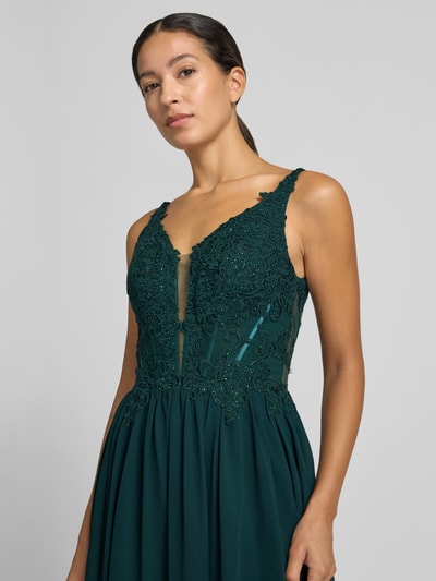 Frauenmodel trägt Abendkleid mit Strasssteinbesatz von LUXUAR FASHION in dunklem Grün mit floraler Spitze und tiefem V-Ausschnitt, Nahaufnahme Oberkörper.
