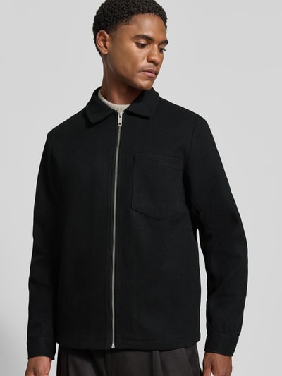 Männermodel trägt Jacke mit Brusttasche und Kentkragen Modell 'ROLFSTED' von Casual Friday in Schwarz, glatte Textur, Ganzkörperansicht von vorne. Gerader Schnitt, Reißverschluss, klassische Details, Kontext: Rückenlänge 62 cm, Schulterbreite 42 cm, Brustweite 51 cm, Ärmellänge 66 cm.