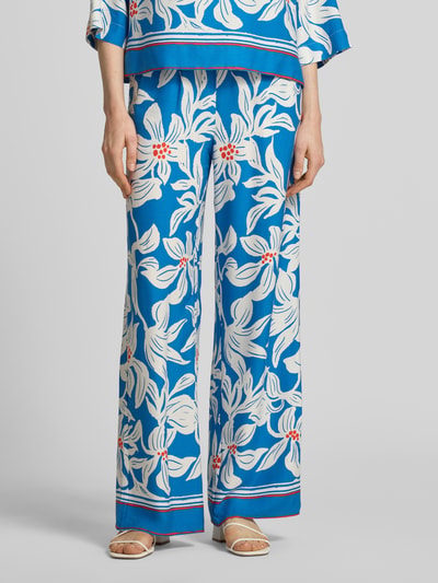 Vrouwenmodel draagt stoffen broek van viscose model 'Rylie' van GUIDO MARIA KRETSCHMER WOMAN, relaxed fit, all-over look, elastische band, blauw met witte bloemen, bandwijdte maat 36: 36 cm, binnenbeenlengte maat 36: 77 cm. Nahaufnahme onderlichaam.