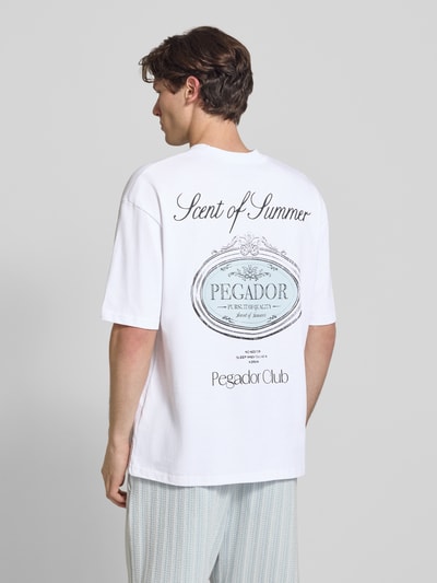 Męski model nosi Oversized T-Shirt mit Label-Print Modell 'Ramon' von PEGADOR z bawełny, okrągły dekolt, długość tyłu 70 cm, Ganzkörperansicht Rückansicht.