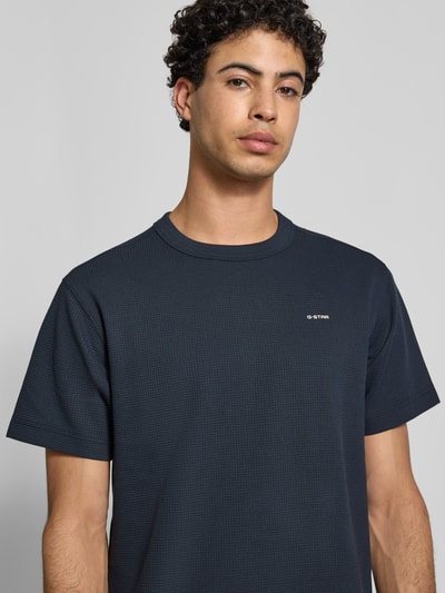 Mannenmodel draagt Regular Fit T-shirt met structuurpatroon van G-Star Raw in donkerblauw, ronde hals, logoprint, heren, nahaufnahme bovenlichaam. Ruglengte bij maat M: 71 cm.