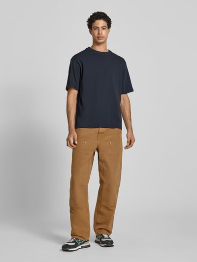 Männermodel trägt Oversized T-Shirt Modell 'FISHER' von Blend in Dunkelblau zu brauner Hose, reine Baumwolle, Ganzkörperansicht von vorne.