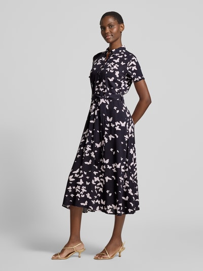 Frauenmodel trägt Hemdblusenkleid im Allover-Look mit Bindegürtel von Christian Berg Woman Selection aus Viskose, taillierter Schnitt, Midikleid, dunkler Grundton mit hellem Muster, Knopfleiste, kurze Ärmel, Ganzkörperansicht von vorne.