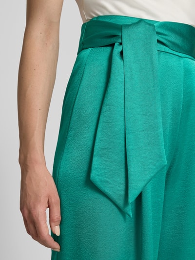 Frauenmodel trägt Relaxed Fit Anzughose aus Satin von Marc Cain in Türkisgrün mit Crinkle-Optik und breitem Stoffgürtel, Nahaufnahme Oberkörper.