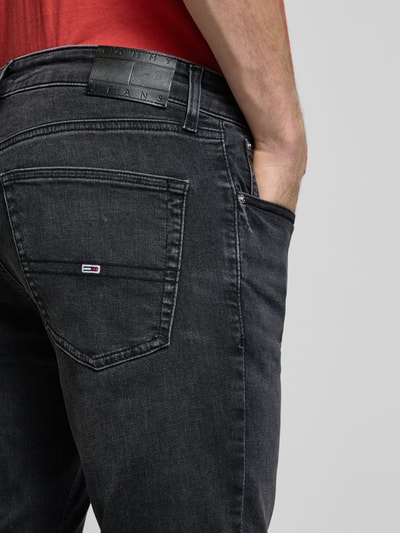 Männermodel trägt Slim Fit Jeans aus Baumwoll-Mix Modell 'AUSTIN' von Tommy Jeans in schwarzer Denim-Optik mit Label-Patch, Detailaufnahme Rückansicht.