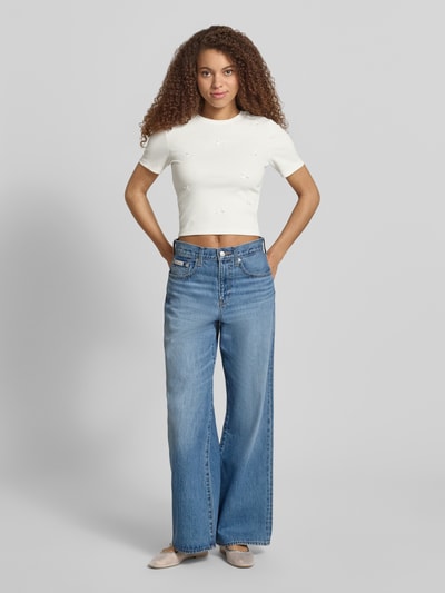 Frauenmodel trägt Slim Fit T-Shirt aus Baumwoll-Mix Modell 'FEMKE' von Only, unifarben, kurzarm, Schleifen-Details, Feinripp, Ganzkörperansicht von vorne.