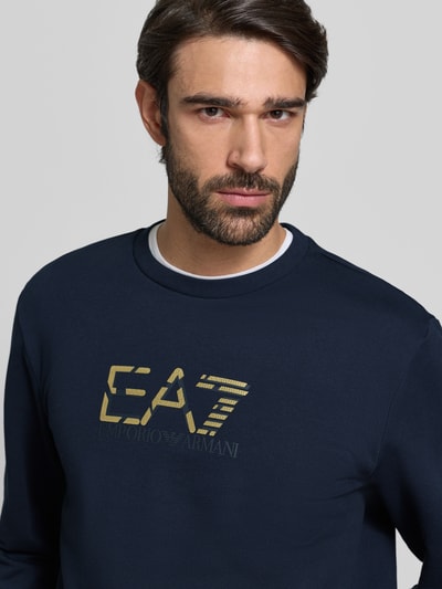 Männermodel trägt Sweatshirt mit Logo und Rundhalsausschnitt von EA7 Emporio Armani in Dunkelblau, reine Baumwolle, Nahaufnahme Oberkörper.
