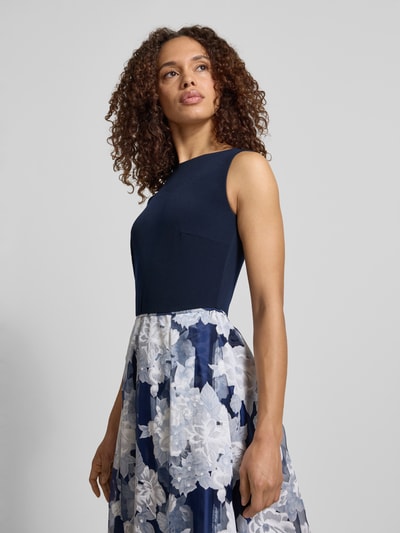 Frauenmodel trägt Abendkleid mit rückseitigem V-Ausschnitt von Christian Berg Cocktail, Dunkelblau, Material-Mix mit Stretch-Anteil, Taillierter Schnitt, Maxikleid, U-Boot-Ausschnitt, floraler Rock in Weiß und Blau, Ganzkörperansicht von vorne. Rückenlänge bei Größe 36: 130 cm, Brustweite bei Größe 36: 47 cm.