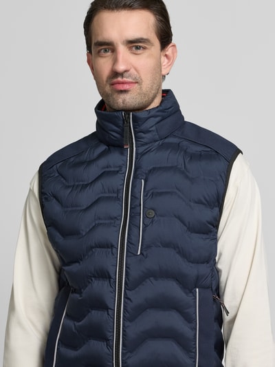 Männermodel trägt Regular Fit Steppweste mit Kapuze im Kragen von Tom Tailor, dunkelblau, Stehkragen, Reißverschluss, Nahaufnahme Oberkörper.