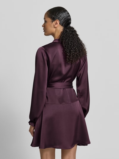 Frauenmodel trägt knielanges Kleid in Wickel-Optik Modell 'Colbie' von Neo Noir aus bordeauxfarbenem Satin, tailliert, Ganzkörperansicht Rückansicht.