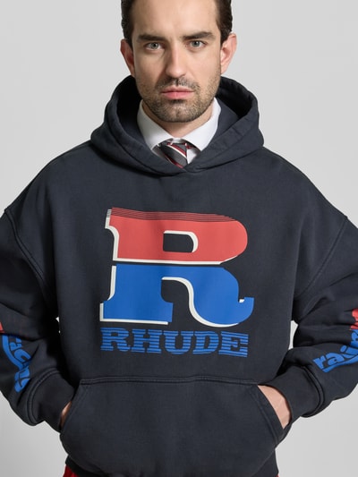 Männermodel trägt Oversized Hoodie aus Baumwolle von RHUDE in Dunkelblau mit Label-Print, Känguru-Tasche und elastischen Abschlüssen, Nahaufnahme Oberkörper. Herren Modell, Rückenlänge bei Größe M: 65 cm.