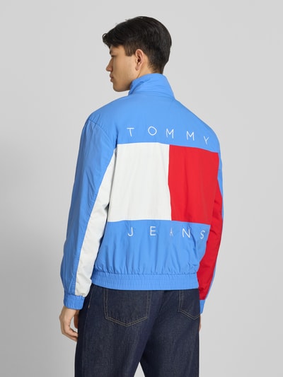 Männermodel trägt Regular Fit Blouson mit Logo-Stitching von Tommy Hilfiger in Optik: Unifarben, Farben Blau, Rot, Weiß, Ganzkörperansicht Rückansicht. Materialverarbeitung: Satin, elastischer Ärmelabschluss und Rumpfabschluss, seitliche Eingrifftaschen mit Druckknopf.