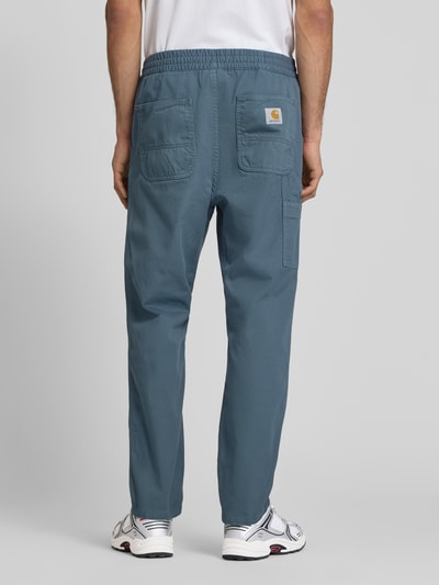 Männermodel trägt Hose mit elastischem Bund Modell 'Moraga' von Carhartt Work In Progress in Blau, Reine Baumwolle, Regular-Fit, Gesäßtaschen, Ganzkörperansicht Rückansicht.