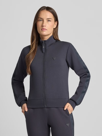 Frauenmodel trägt Regular Fit Sweatjacke aus Viskose-Mix von Guess Activewear in Dunkelgrau mit Stehkragen und Logo, Ganzkörperansicht von vorne.