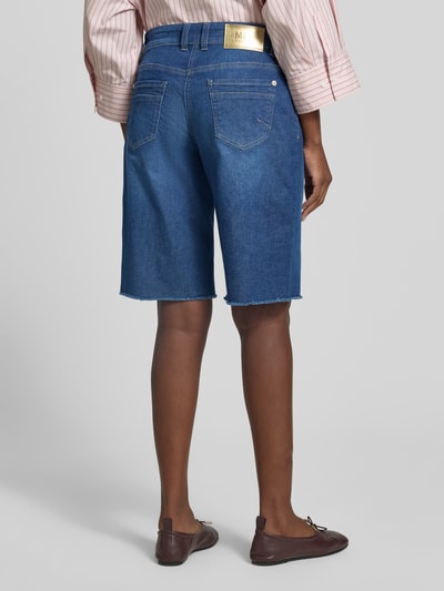 Frauenmodel trägt Jeansshorts mit Fransen Modell 'Rich' von MAC aus Baumwoll-Elasthan-Mix, Relaxed-Fit, Eingrifftaschen, Ganzkörperansicht Rückansicht.