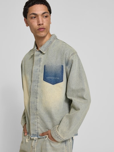 Männermodel trägt Hemdjacke in Denim-Optik von Don't Waste Culture aus reiner Baumwolle, Relaxed-Fit, Statement-Print, Kentkragen, Ganzkörperansicht von vorne.