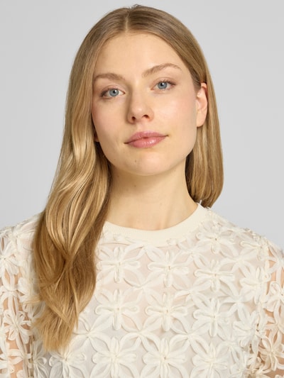Modelka kobieca nosi Blusenshirt mit Stitchings und Puffärmeln od Rich & Royal, kremowy kolor, krój regular fit, okrągły dekolt, długość tyłu 59 cm, długość rękawa 31 cm, zdjęcie zbliżenie górnej części ciała.
