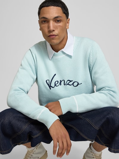 Männermodel trägt Leinenpullover aus Leinen-Mix von Kenzo in Hellblau mit Kontraststreifen, gerippten Abschlüssen, Label-Stitching, lockerer Passform, Nahaufnahme Oberkörper.