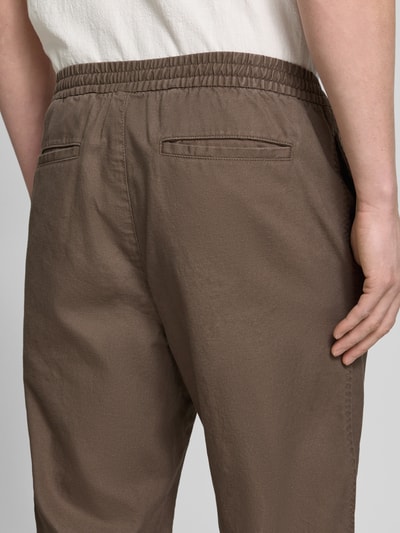 Männermodel trägt Leinenhose mit elastischem Bund und Eingrifftaschen von GAP in Braun, Baumwoll-Leinen-Mix, Gesäßleistentaschen, Nahaufnahme Rückansicht.