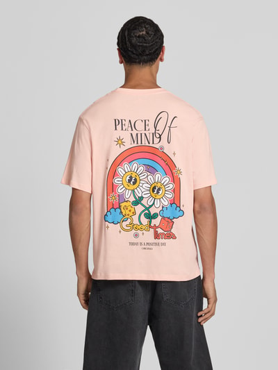 Männermodel trägt T-shirt met motiefprint model 'VINTAGE CARTOON' van Jack & Jones, puur katoen, regular fit, ronde hals, ruglengte maat M 69 cm, lichtroze met kleurrijke print, ganzkörperansicht rugaanzicht.