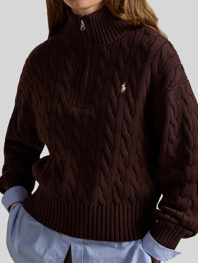 Frauenmodel trägt Troyer mit Zopfstrickmuster von Polo Ralph Lauren in Dunkelbraun, Baumwolle, Stehkragen mit Reißverschluss, Nahaufnahme Oberkörper.