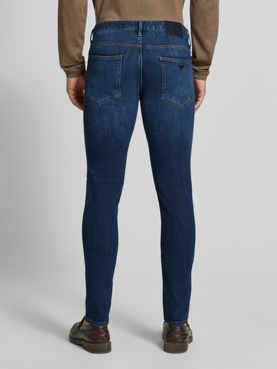 Männermodel trägt Slim Fit Jeans aus Baumwoll-Mix im 5-Pocket Design von Emporio Armani, dunkelblaue Farbe, Rückansicht Ganzkörperansicht. Elastischer Baumwoll-Mix, Knopf- und Reißverschluss, Bundweite 42 cm, Innenbeinlänge 84 cm.